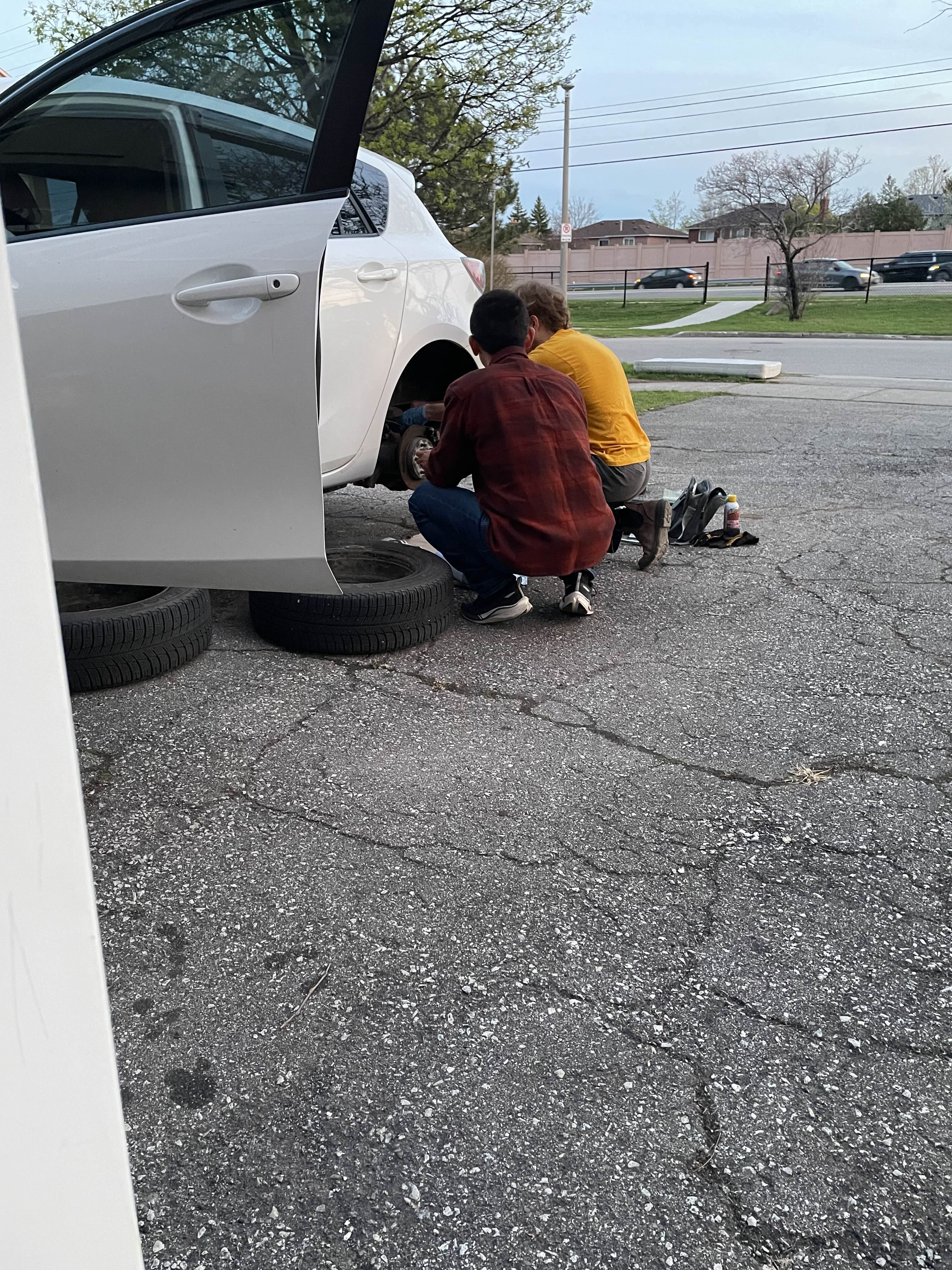 Two people next to car on jack stands